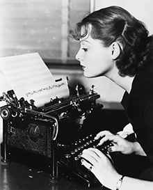 black-and-white photo of woman typing on an old-fashioned typewriter